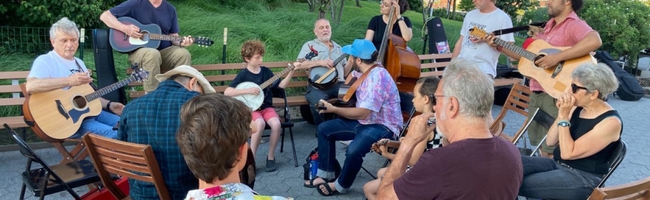 A group of musicians seated on benches at a park, playing various acoustic instruments