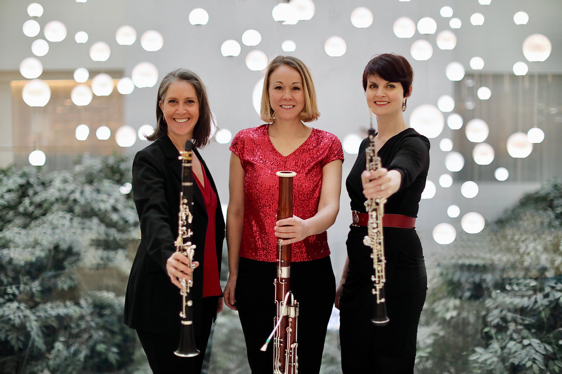 Three women stand in front of a sparkly background, holding wood wind instruments out.